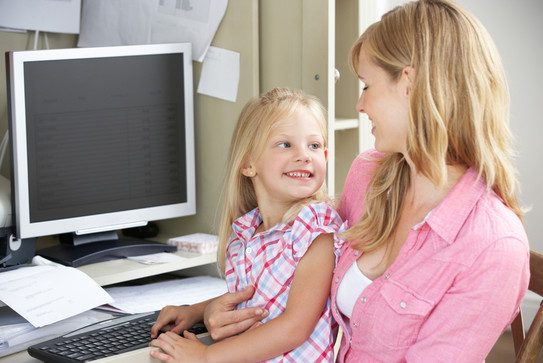 Mutter mit Tochter auf dem Schoß am PC Arbeitsplatz.