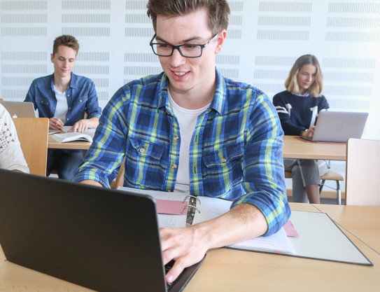 Student Laptop A student is typing on a laptop, two others are sitting behind him.