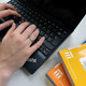 Lernen mit dem Laptop Eine Studentin tippt an einem Laptop und gelbe Bücher legen daneben.