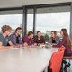 Six students are sitting at a table with books and notepads on.