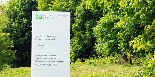 Begrüßungsschild Ein weißes Begrüßungsschild der TU Dortmund steht auf einem grünen Rasen.